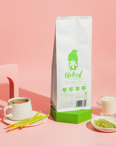 Bag of Matcha Powder (Naked Syrups), sitting next to cup of fresh matcha latte