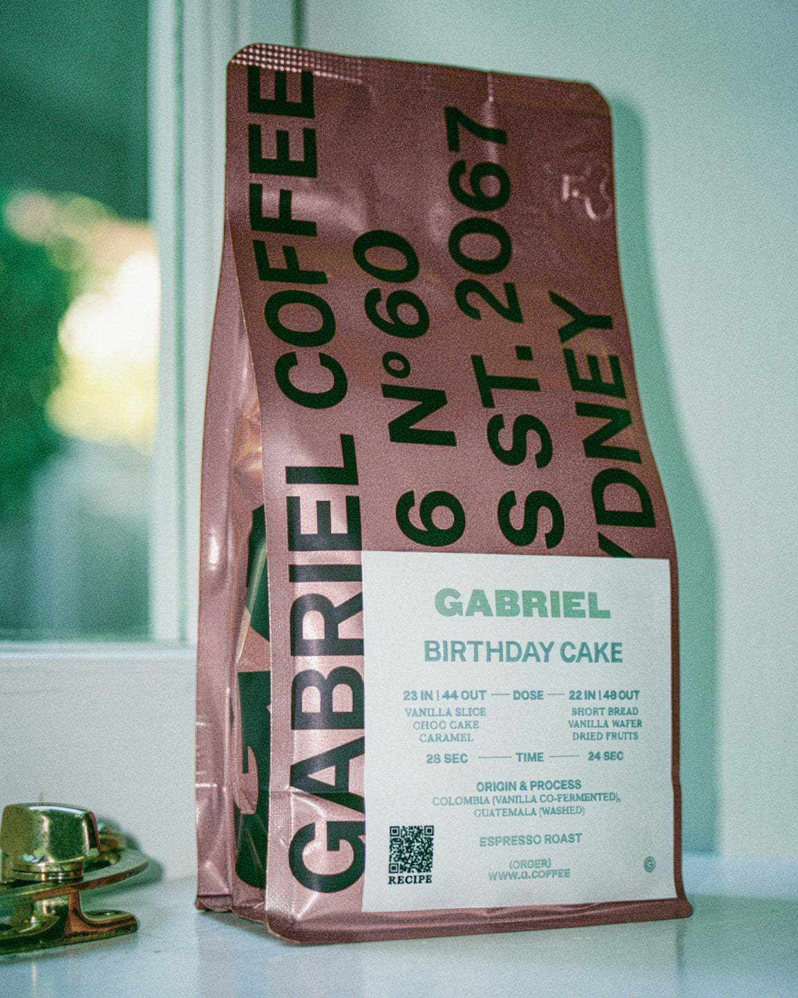 Gabriel Coffee bag labeled 'Birthday Cake' on a reflective surface with a blurred background
