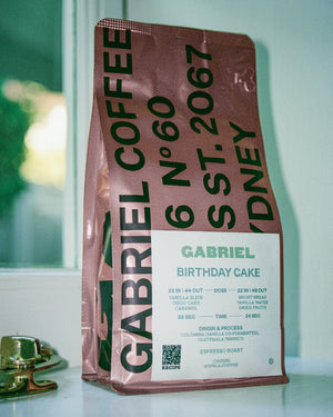 Gabriel Coffee bag labeled 'Birthday Cake' on a reflective surface with a blurred background